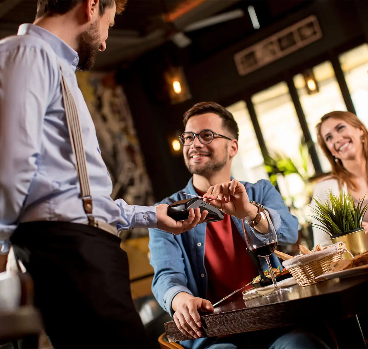 Smiling customer paying with a contactless card using a Mealzo PDQ machine at a modern counter